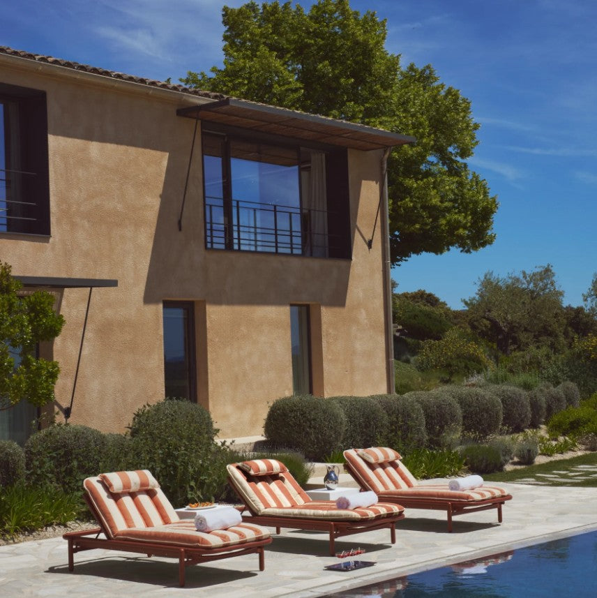 Three striped Sunbun daybeds with white towels rest poolside beside a modern villa.